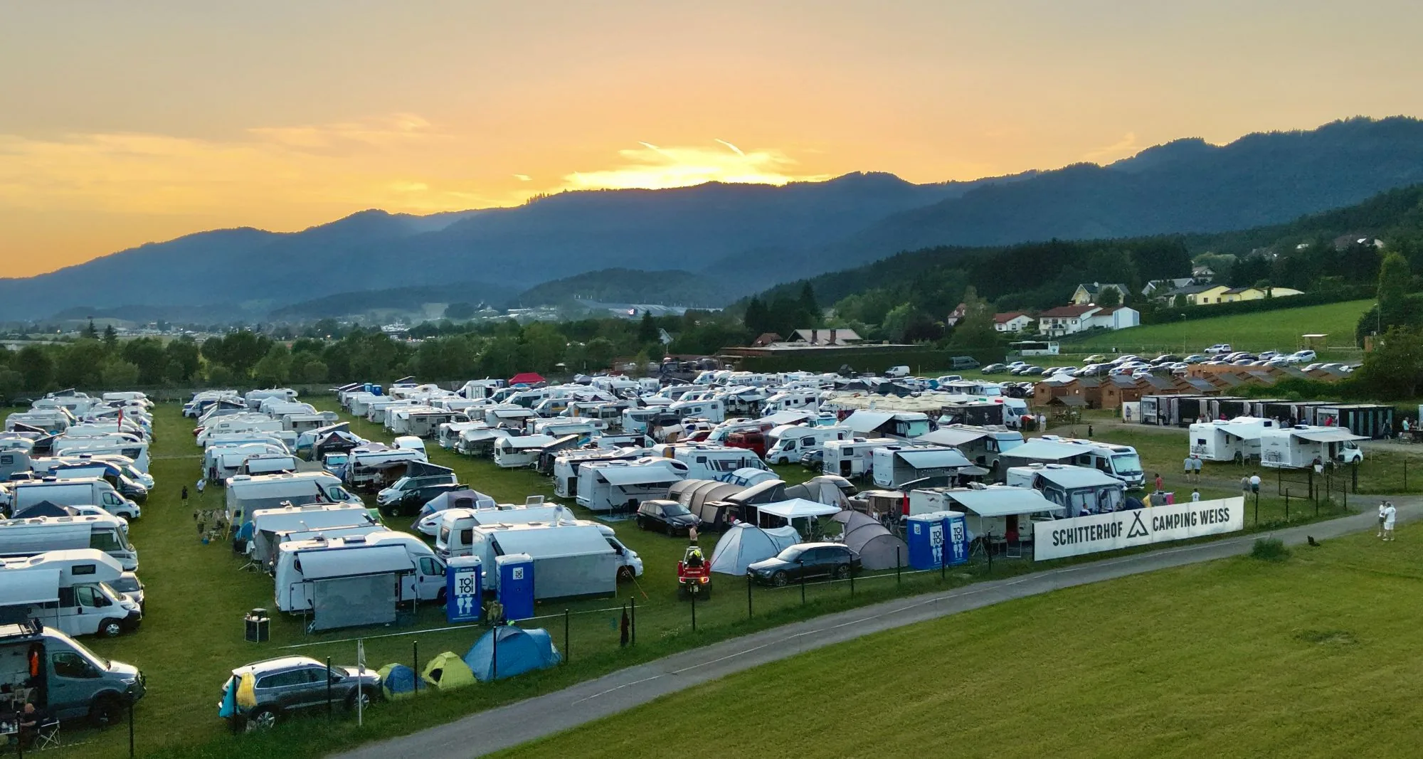 Campingplatz Schitterhof CAMPING WEISS bei Sonnenuntergang: Wohnmobile und Zelte auf der Wiese vor der Bergkulisse des Murtals
